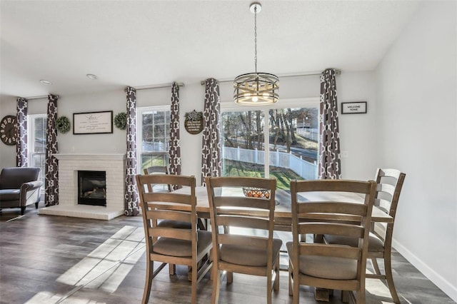 dining area featuring a brick fireplace, dark wood-type flooring, and a chandelier