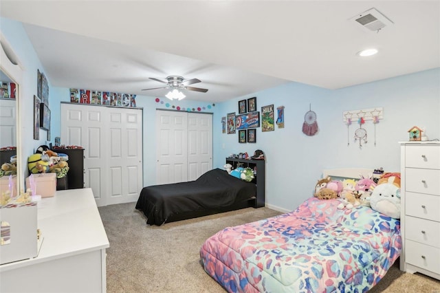 bedroom with ceiling fan, light colored carpet, and two closets