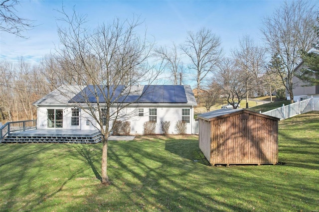 back of property featuring a yard, a wooden deck, a storage unit, and solar panels