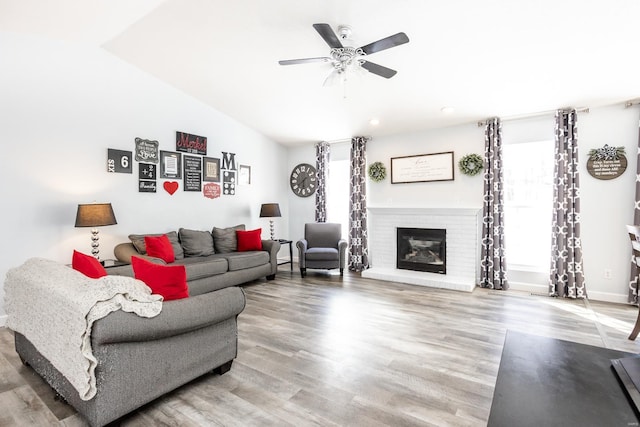 living room featuring ceiling fan, lofted ceiling, hardwood / wood-style flooring, and a brick fireplace