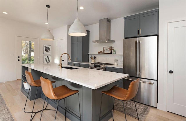 kitchen with hanging light fixtures, stainless steel appliances, wall chimney range hood, a breakfast bar area, and a kitchen island with sink