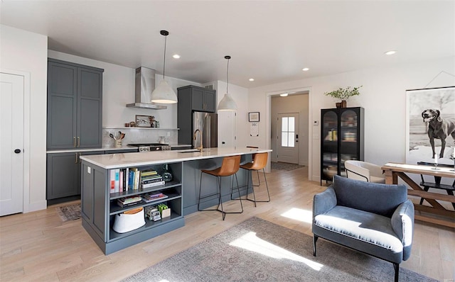 kitchen featuring hanging light fixtures, light hardwood / wood-style flooring, a kitchen island with sink, and wall chimney range hood