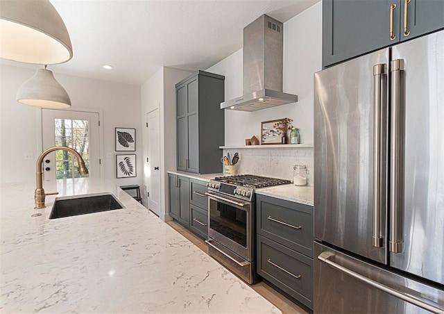 kitchen with light stone countertops, gray cabinetry, sink, wall chimney range hood, and high quality appliances