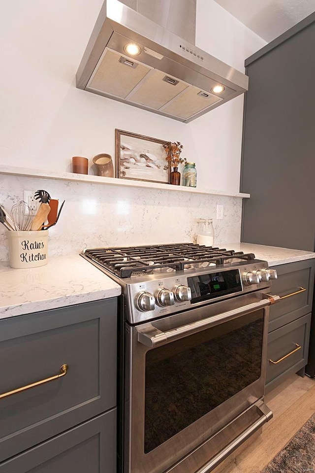 kitchen featuring gray cabinetry, light wood-type flooring, high end stove, range hood, and tasteful backsplash