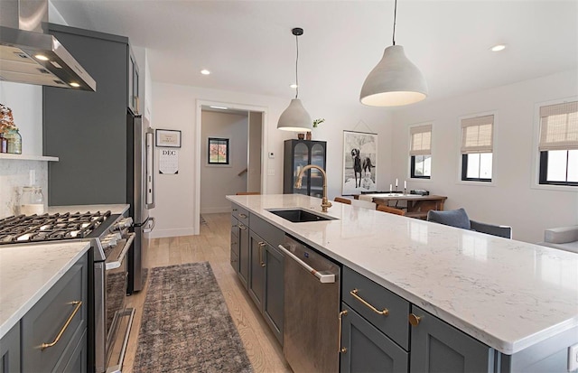 kitchen featuring wall chimney range hood, sink, decorative light fixtures, light hardwood / wood-style floors, and stainless steel appliances