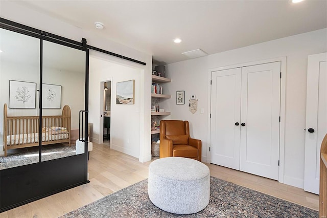 bedroom with light wood-type flooring, a barn door, a nursery area, and a closet