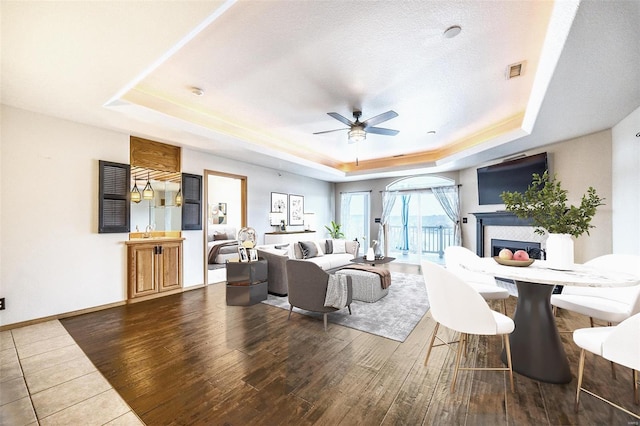 living room featuring a fireplace, dark hardwood / wood-style flooring, a raised ceiling, and ceiling fan