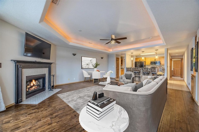 living room featuring a raised ceiling, a tile fireplace, ceiling fan, and hardwood / wood-style floors