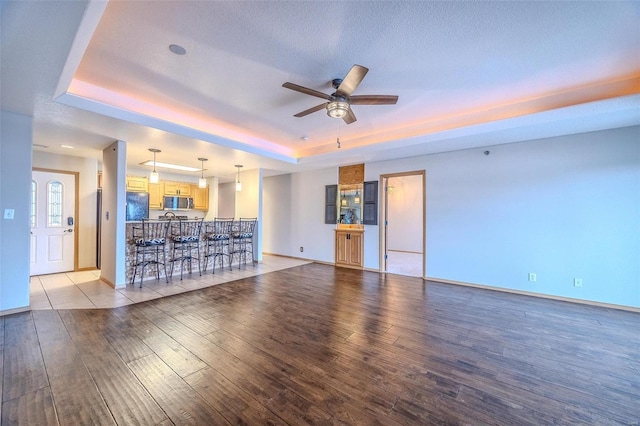 unfurnished living room with a tray ceiling, ceiling fan, light hardwood / wood-style floors, and a textured ceiling