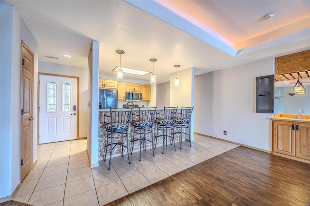 kitchen with light brown cabinetry, black fridge, sink, light hardwood / wood-style floors, and hanging light fixtures