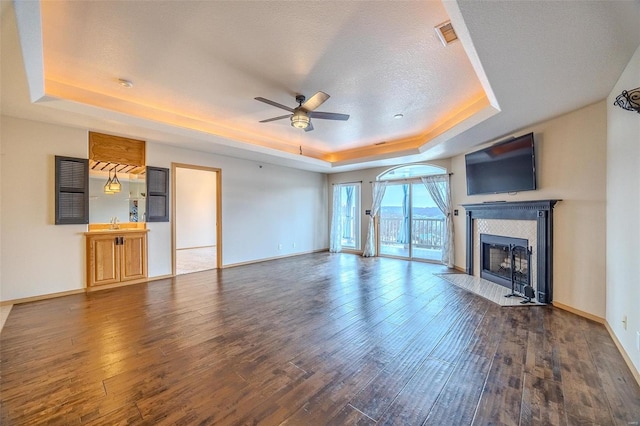 unfurnished living room with a raised ceiling, ceiling fan, a textured ceiling, dark hardwood / wood-style flooring, and a tiled fireplace