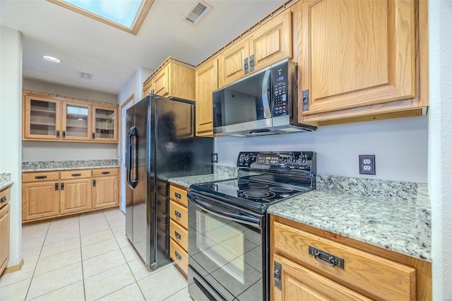 kitchen featuring light stone countertops, light tile patterned floors, a skylight, and black appliances