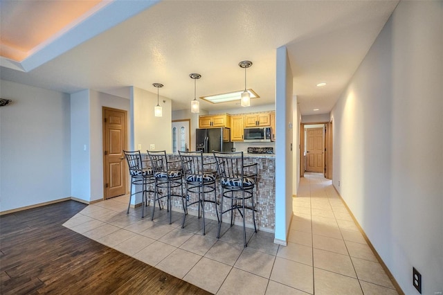 kitchen featuring light brown cabinetry, a kitchen breakfast bar, black fridge with ice dispenser, light hardwood / wood-style flooring, and hanging light fixtures