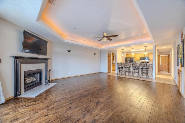 unfurnished living room with a fireplace, ceiling fan, light hardwood / wood-style flooring, and a tray ceiling