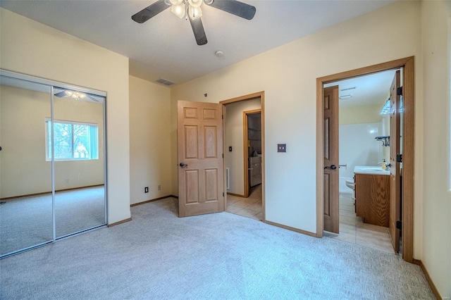 unfurnished bedroom with light carpet, ensuite bath, a closet, and ceiling fan