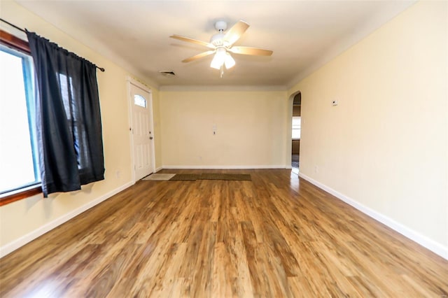 unfurnished room with arched walkways, ceiling fan, wood finished floors, visible vents, and baseboards