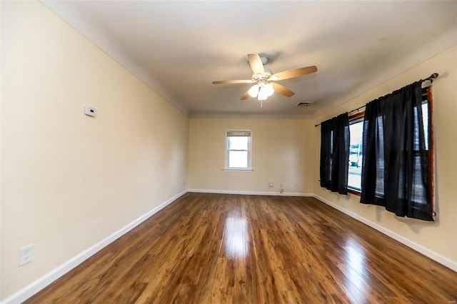 spare room featuring dark wood-type flooring, visible vents, baseboards, and a ceiling fan