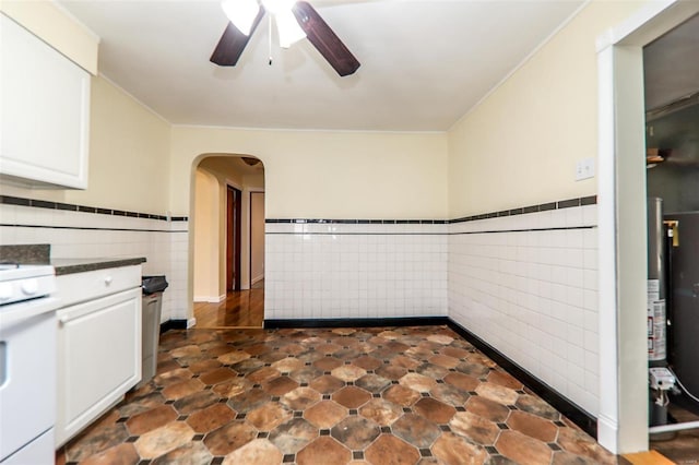 kitchen with arched walkways, tile walls, dark countertops, white cabinets, and white stove