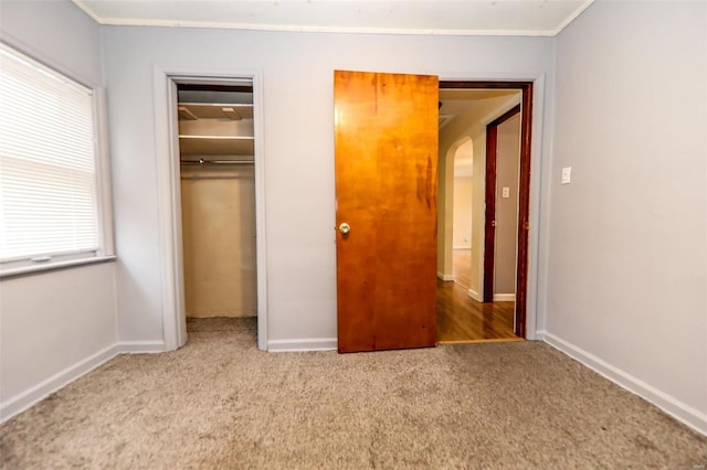 unfurnished bedroom with carpet floors, multiple windows, arched walkways, and a closet