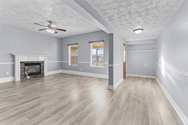 unfurnished living room with a textured ceiling, light hardwood / wood-style floors, a stone fireplace, and ceiling fan