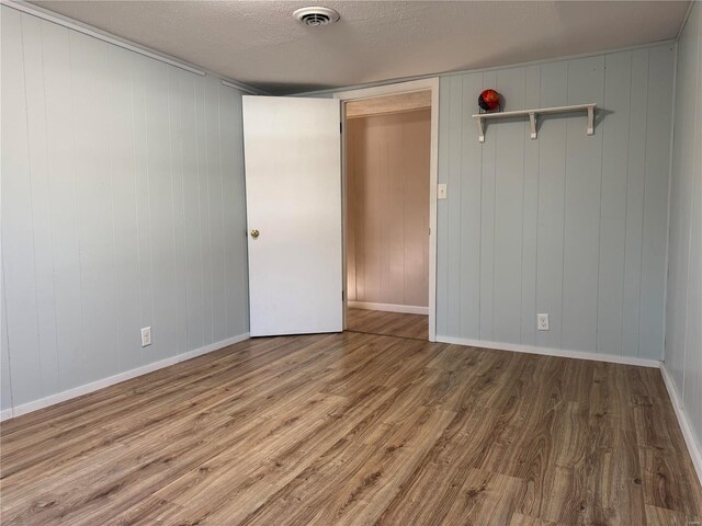 spare room with wood walls, wood-type flooring, and a textured ceiling