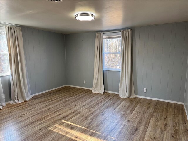 empty room with light wood-type flooring and wooden walls