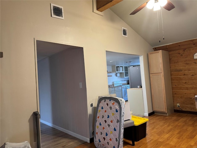 sitting room with ceiling fan, beam ceiling, high vaulted ceiling, hardwood / wood-style floors, and wood walls