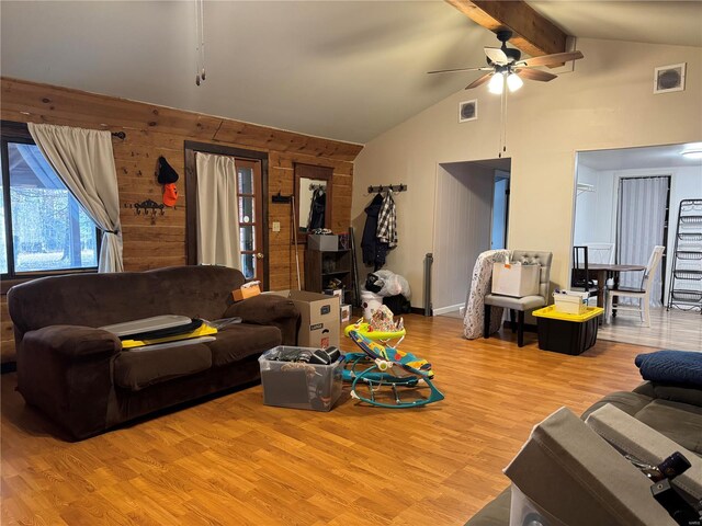 living room with wooden walls, ceiling fan, lofted ceiling with beams, and light wood-type flooring