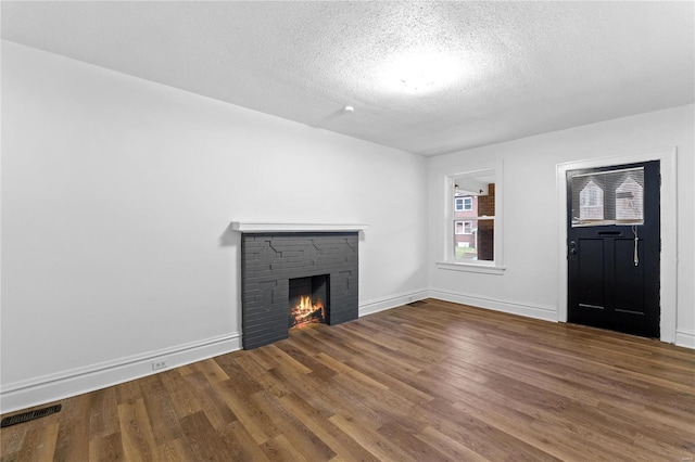 unfurnished living room featuring a textured ceiling, hardwood / wood-style flooring, and a stone fireplace