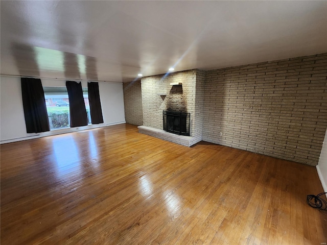 unfurnished living room with hardwood / wood-style flooring, a brick fireplace, and brick wall