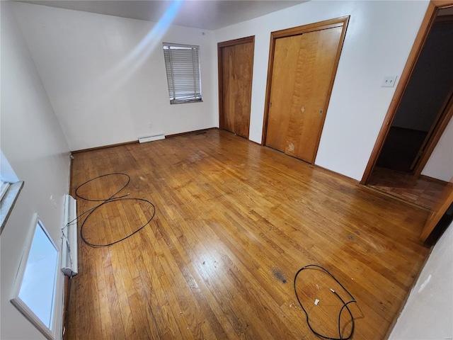 unfurnished bedroom with multiple closets, light hardwood / wood-style flooring, basketball court, and a baseboard radiator