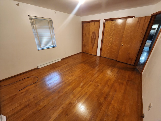 unfurnished bedroom with hardwood / wood-style floors, baseboard heating, and multiple closets