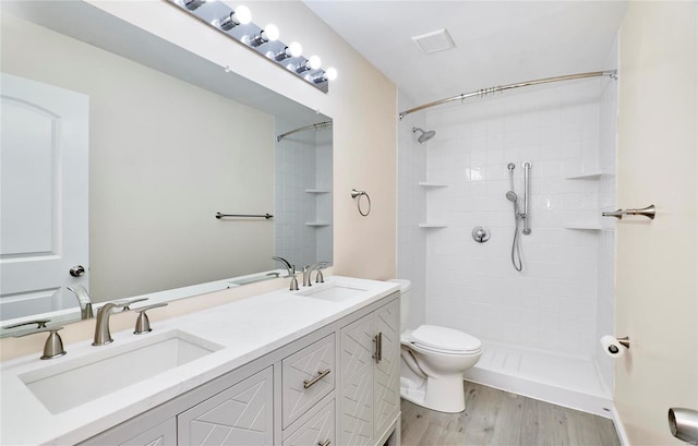 bathroom with toilet, wood finished floors, a sink, a shower stall, and double vanity