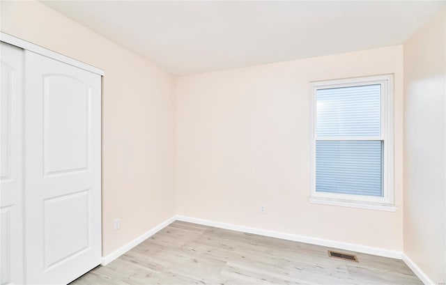 spare room featuring light wood-type flooring, visible vents, and baseboards