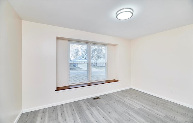 empty room featuring light wood-type flooring, visible vents, and baseboards