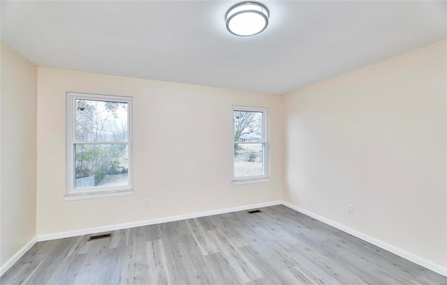 empty room with light wood finished floors, visible vents, and baseboards