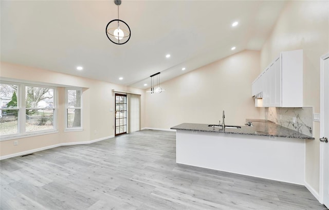 kitchen featuring hanging light fixtures, light hardwood / wood-style flooring, vaulted ceiling, dark stone countertops, and white cabinetry