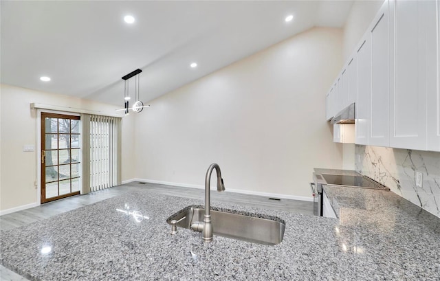 kitchen featuring white cabinets, hanging light fixtures, vaulted ceiling, stone counters, and a sink