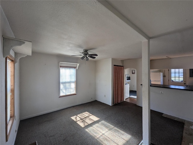 unfurnished living room featuring ceiling fan, a textured ceiling, and dark colored carpet