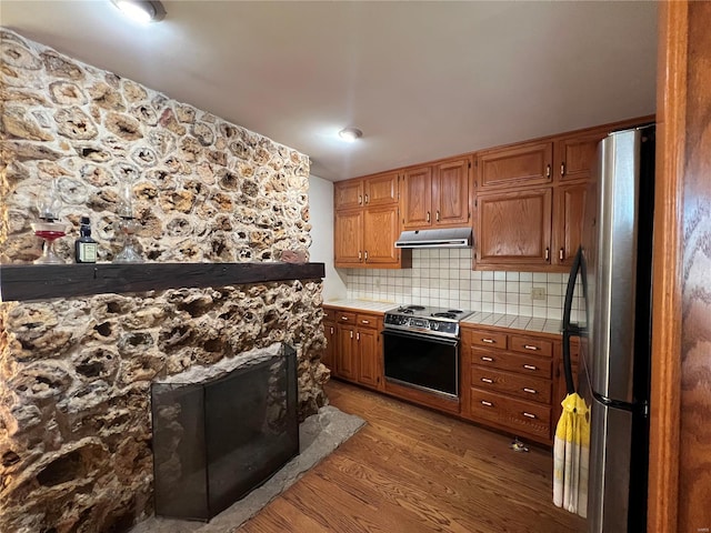 kitchen with hardwood / wood-style floors, stove, decorative backsplash, stainless steel fridge, and tile counters