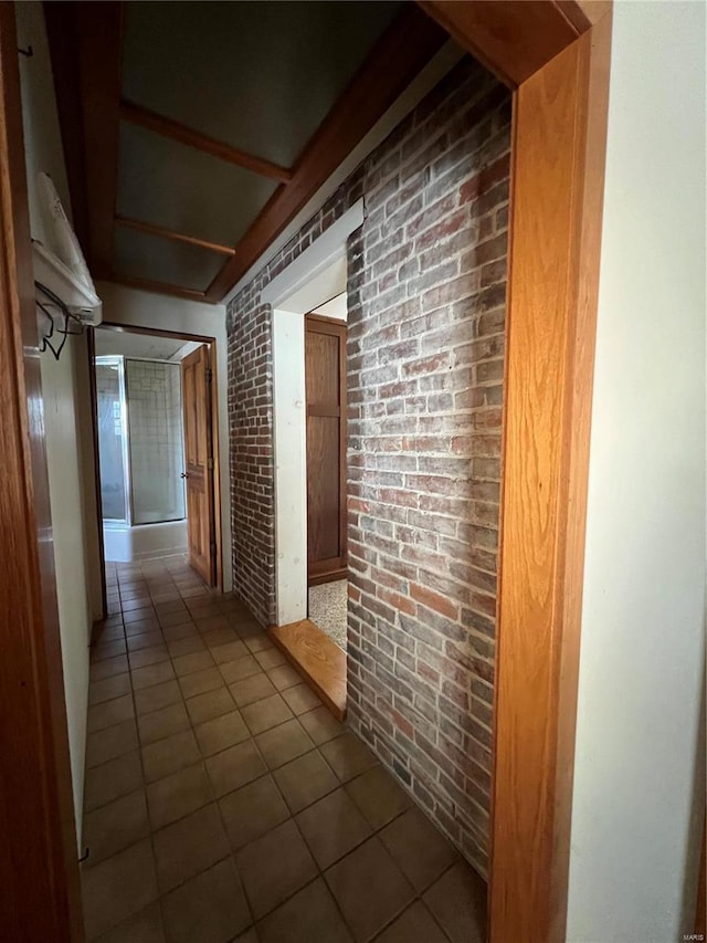 corridor featuring dark tile patterned floors and brick wall