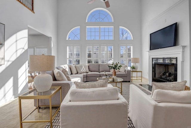 living room featuring ceiling fan, light colored carpet, a towering ceiling, and a premium fireplace