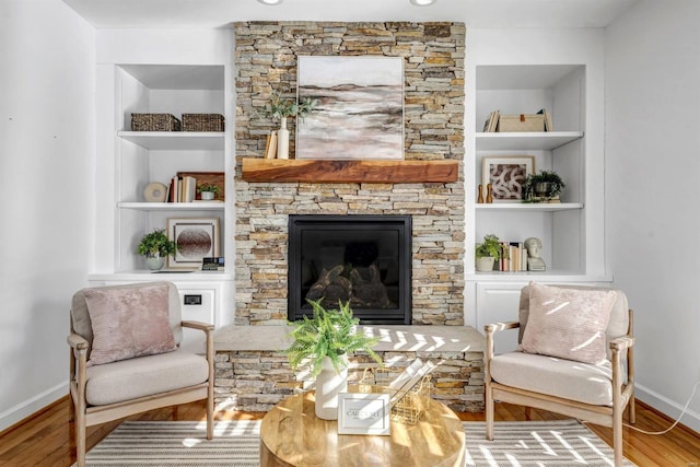 sitting room featuring built in features, hardwood / wood-style floors, and a stone fireplace