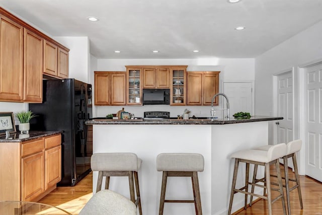 kitchen featuring an island with sink, dark stone counters, black appliances, light hardwood / wood-style flooring, and sink