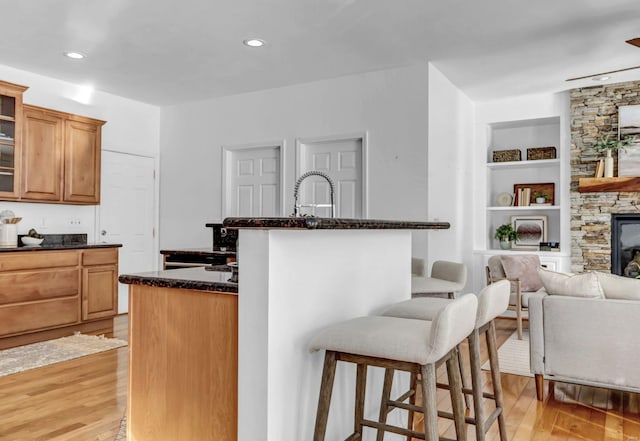 kitchen with dark stone countertops, a fireplace, a kitchen breakfast bar, built in features, and light hardwood / wood-style flooring