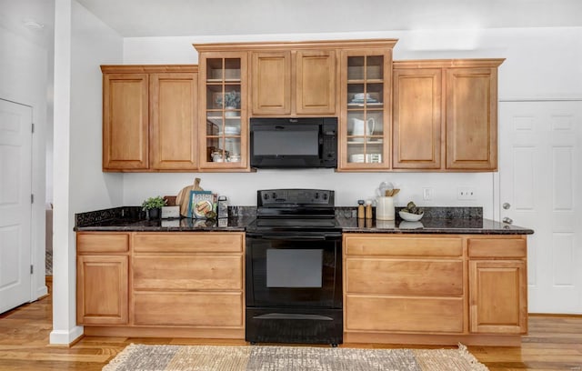 kitchen with dark stone countertops, light hardwood / wood-style floors, and black appliances