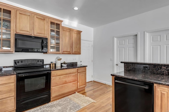 kitchen featuring light wood-type flooring, light brown cabinets, dark stone counters, and black appliances