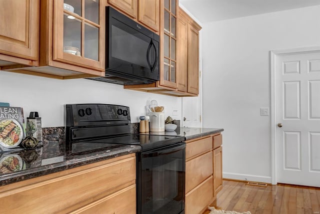 kitchen featuring dark stone countertops, light hardwood / wood-style floors, and black appliances