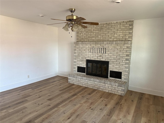 unfurnished living room featuring wood-type flooring, a brick fireplace, and ceiling fan