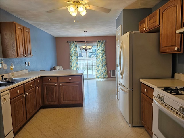 kitchen with white appliances, ceiling fan with notable chandelier, sink, hanging light fixtures, and kitchen peninsula